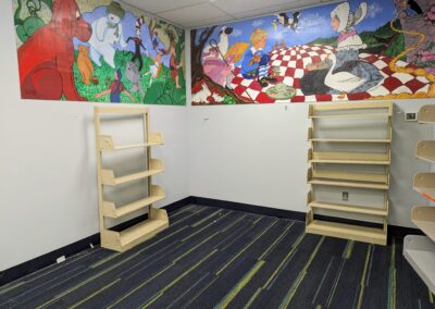 Empty shelves in the old picture book area of the children's room with a mural above