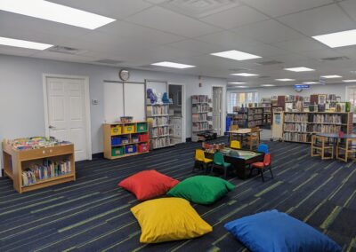 Shelving in the children's area of the library with tables, chairs, large bright pillows, and plastic toy bins