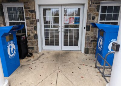 the front doors of the library showing the children's return bin on the left and the adult/young adult bin on the right.